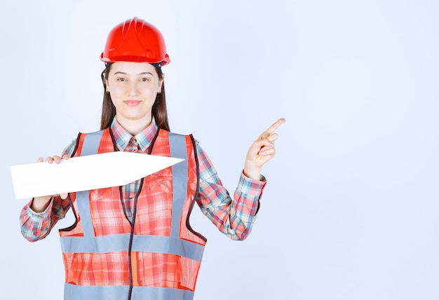 Engenheira em capacete vermelho, segurando uma seta apontando para a direita.