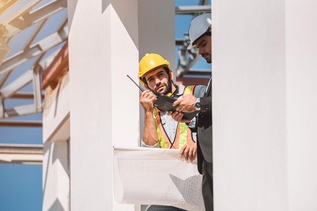 Engenheiro civil e gerente de trabalhadores da construção civil segurando tablet digital e plantas falando e planejando sobre o conceito de trabalho em equipe de cooperação no canteiro de obras