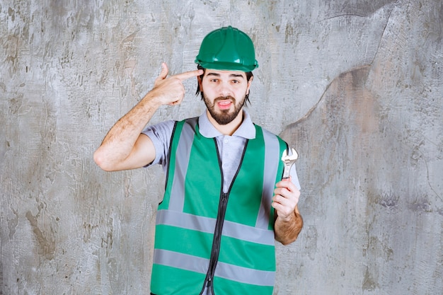 Foto grátis engenheiro com equipamento amarelo e capacete segurando uma chave metálica e parece confuso e pensativo.