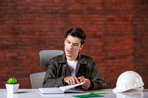 Engenheiro de frente, sentado atrás de seu local de trabalho, listando o caderno de empregos empreiteiro agenda plano de propriedade construtor corporativo