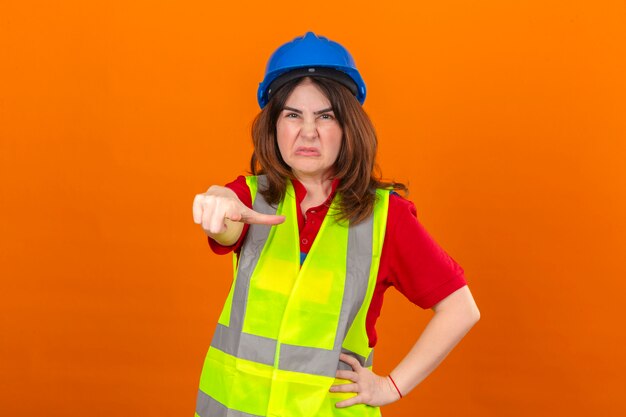 Engenheiro de mulher vestindo colete de construção e capacete de segurança apontando descontente e frustrado para a câmera com raiva e furioso com você sobre parede laranja isolada