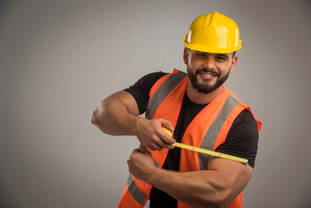 Engenheiro de uniforme laranja e capacete amarelo com régua.