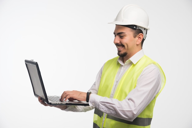 Engenheiro de uniforme segurando um laptop e escrevendo.