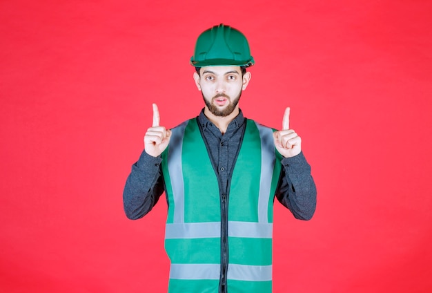 Engenheiro de uniforme verde e capacete apontando acima.