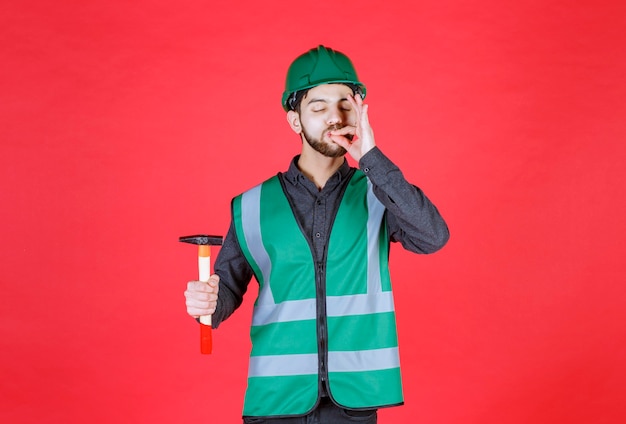 Engenheiro de uniforme verde e capacete segurando um machado de madeira e mostrando sinal positivo com a mão.
