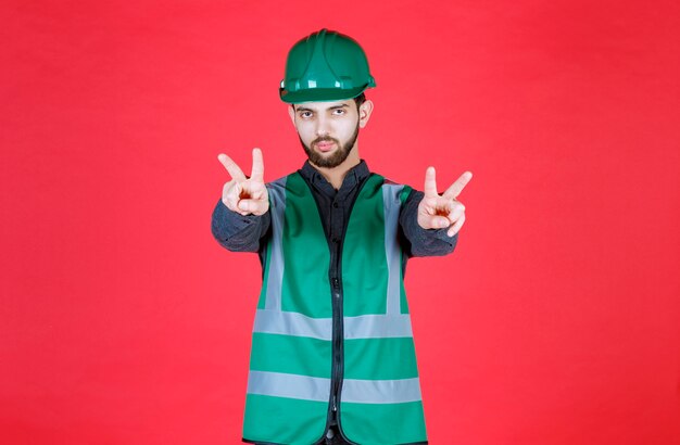 Foto grátis engenheiro de uniforme verde e capacete transmitindo paz e amizade.