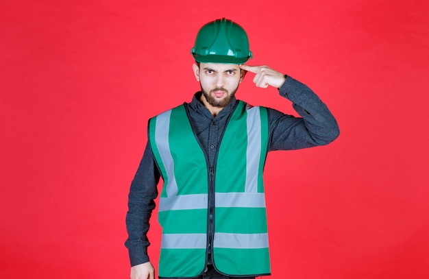Engenheiro de uniforme verde e pensamento e planejamento de capacete.