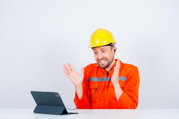 Engenheiro feliz está segurando as mãos sentado na frente de seu tablet no fundo branco