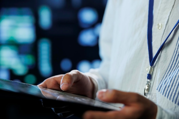 Engenheiro no centro de dados usando tablet para evitar sobrecarga do sistema de perto empregado na sala de servidores garantindo que haja conectividade de rede suficiente para operações suaves fundo desfocado