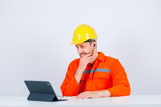 Engenheiro sorridente está colocando a mão no queixo sentado na frente de seu tablet no fundo branco