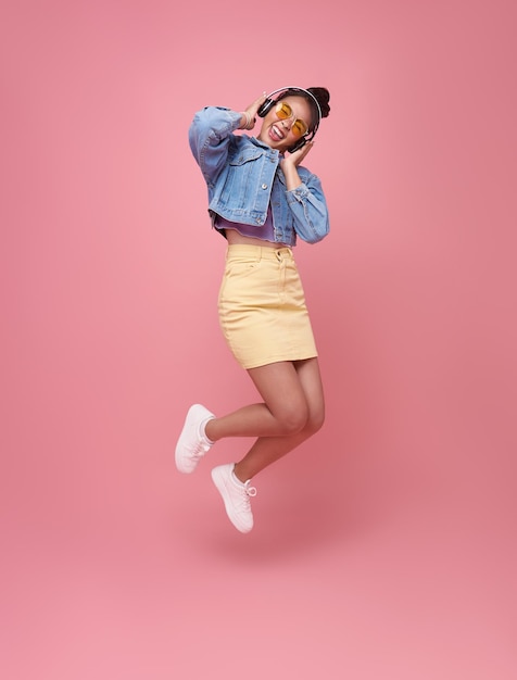 Foto grátis engraçada jovem asiática pulando retrato de estúdio ouvindo música com fones de ouvido dançando