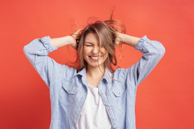 Engraçado, linda garota se divertindo enquanto brincava com o cabelo isolado em uma parede vermelha