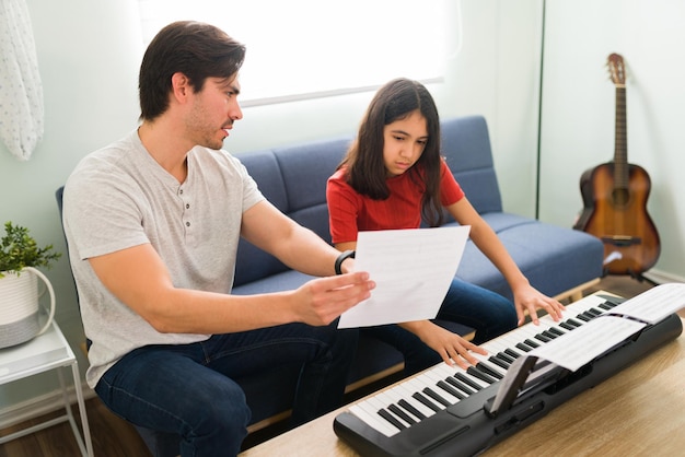 Ensinar a ler uma partitura. criança hispânica aprendendo a tocar piano com a ajuda de um professor de música masculino durante as aulas em casa