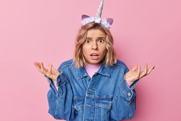 Foto grátis então, o que vem a seguir mulher indignada chocada mantém as palmas das mãos levantadas encolhe os ombros usa jaqueta jeans de bandana de unicórnio não consegue entender algo isolado sobre parede rosa expressa indignação ou ressentimento