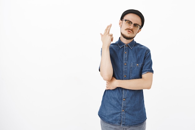 Entediado farto de homem bonito e elegante com bigode e barba em um gorro preto inclinando a cabeça para longe de um gesto de arma de dedo levantado perto da cabeça como se estivesse explodindo ou atirando de tédio