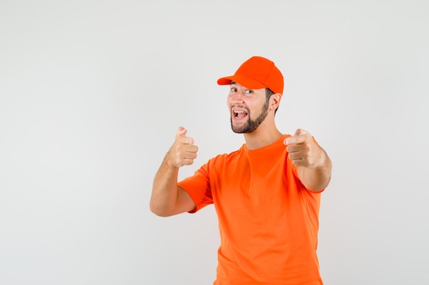 Entregador, apontando em t-shirt laranja, boné e parecendo feliz, vista frontal.