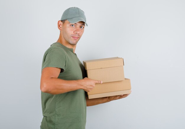 Entregador, apontando o dedo para caixas de papelão em t-shirt verde, boné.