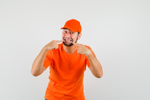 Entregador, apontando para os dentes em t-shirt laranja, vista frontal do boné.