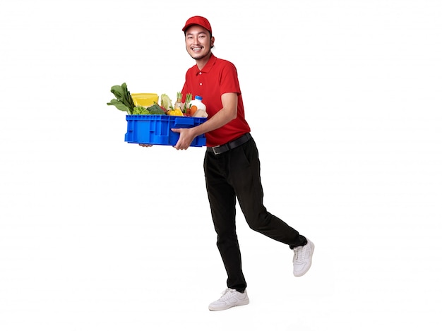 Entregador asiático vestindo uniforme vermelho, segurando uma cesta de alimentos frescos isolada no espaço em branco. serviço de entrega expressa.