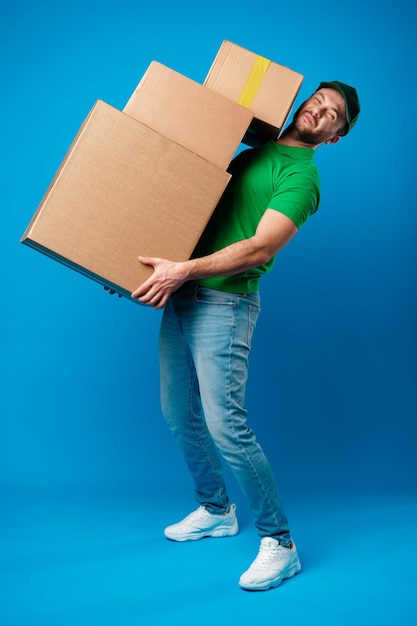 Foto grátis entregador com enorme pilha de caixas contra fundo azul