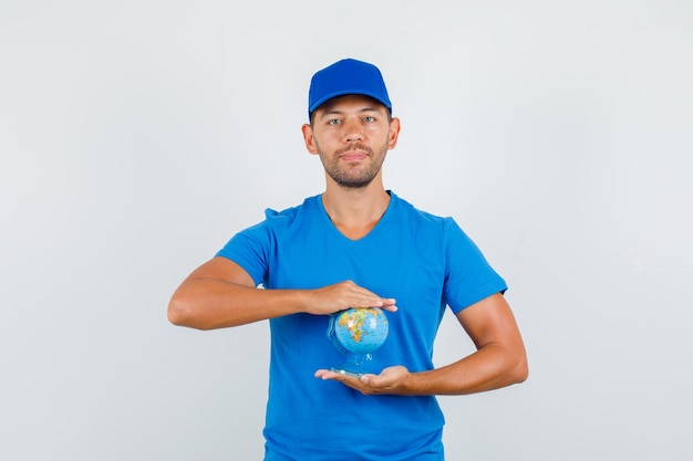 Entregador de camiseta azul, boné segurando um globo e parecendo positivo