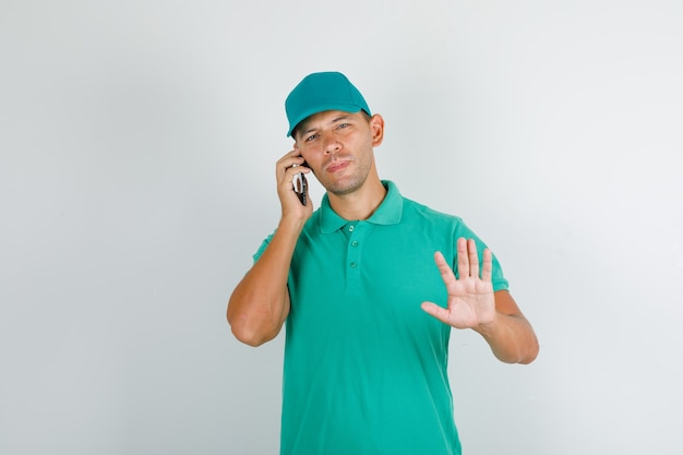 Entregador de camiseta verde com boné falando ao telefone com placa de pare