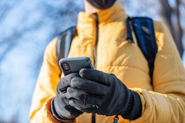 Entregador de comida com mochila usando seu smartphone. Jaqueta amarela e luvas pretas. Inverno