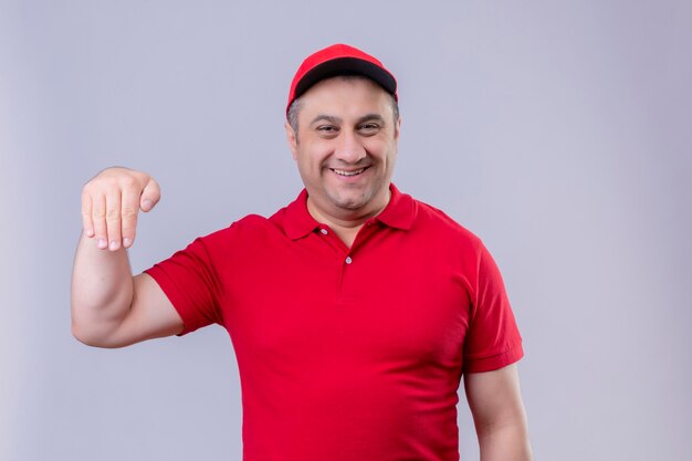 Entregador de uniforme vermelho e boné gesticulando com a mão sorrindo conceito de linguagem corporal em pé