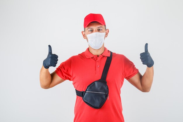 Entregador de uniforme vermelho, máscara médica, luvas mostrando os polegares para cima e parecendo positivo