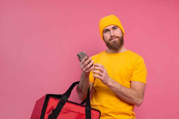 Entregador europeu alegre com bolsa casual segurar telefone rosa