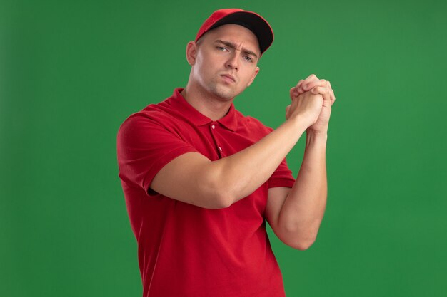 Entregador jovem confiante vestindo uniforme e boné mostrando gesto de aperto de mão isolado na parede verde