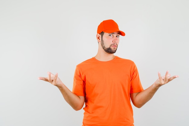 Entregador, mantendo as mãos, mostrando um gesto perplexo em t-shirt laranja, boné, vista frontal.