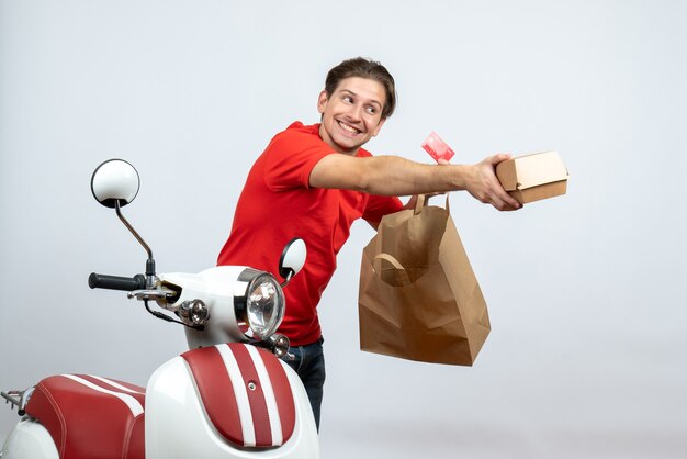 Entregador ocupado em uniforme vermelho em pé perto da scooter e segurando pedidos de cartão do banco sobre fundo branco