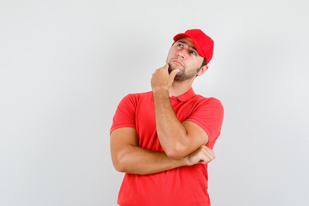 Foto grátis entregador olhando para cima enquanto toca o queixo com camiseta vermelha