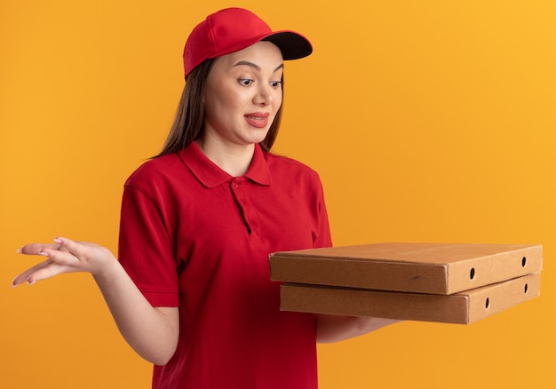 Entregadora bonita animada de uniforme segurando e olhando para caixas de pizza