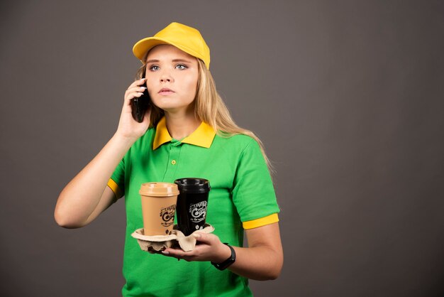 Entregadora com xícaras de café, falando no smartphone.