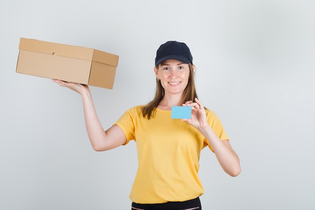 Entregadora de camiseta, calça, boné segurando caixa de papelão e cartão azul