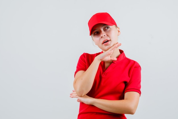 Entregadora de camiseta vermelha e boné apoiando a mão no queixo e parecendo pensativa