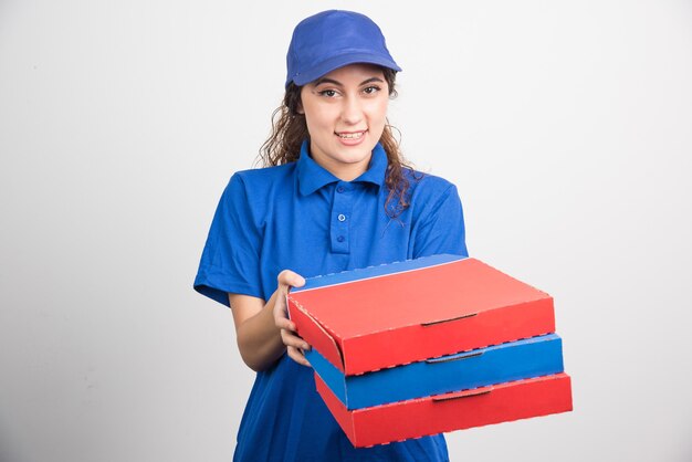 Entregadora de pizza segurando três caixas em fundo branco. Foto de alta qualidade