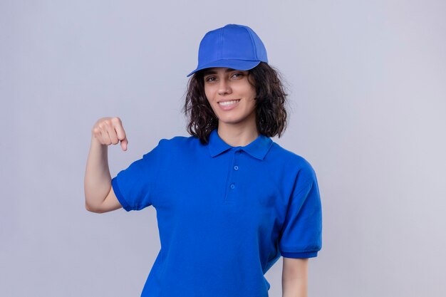 Entregadora de uniforme azul e boné sorrindo amigável gesticulando com o punho como se cumprimentando, aprovando ou como sinal de respeito, de pé sobre um espaço em branco isolado