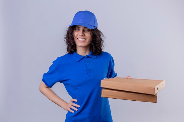 Entregadora de uniforme azul segurando caixas de pizza positiva e feliz sorrindo amigável em pé no branco isolado