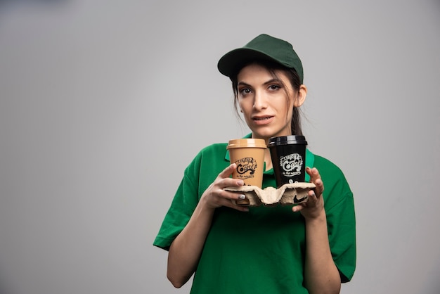 Entregadora de uniforme verde em pé com xícaras de café.