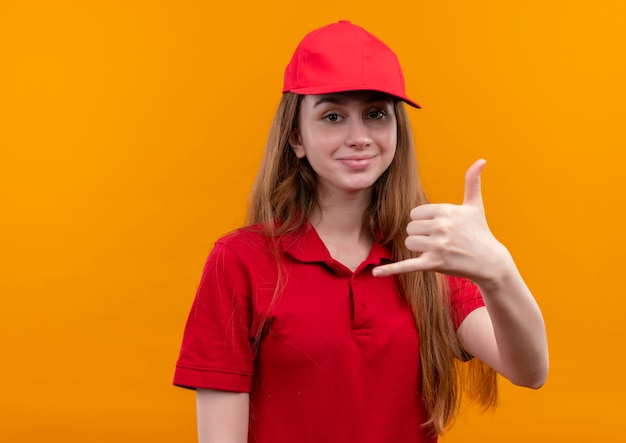 Entregadora jovem confiante em uniforme vermelho fazendo um gesto de chamada em um espaço laranja isolado com espaço de cópia