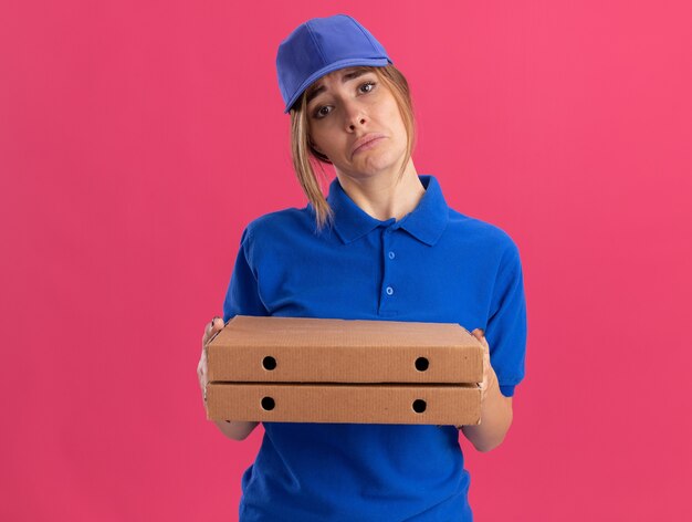 Entregadora jovem e triste de uniforme segurando caixas de pizza rosa