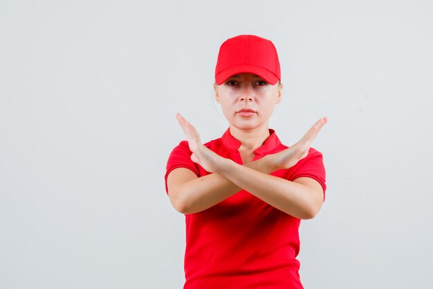 Entregadora mostrando gesto de pare em camiseta vermelha e boné e parecendo rigoroso