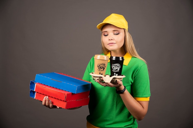 Entregadora olhando xícaras de café e segurando cartolinas de pizza.