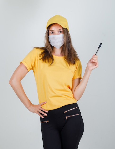 Entregadora posando segurando uma caneta com camiseta, calça, boné e máscara