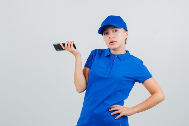 Entregadora segurando um celular com a mão na cintura com camiseta azul e boné