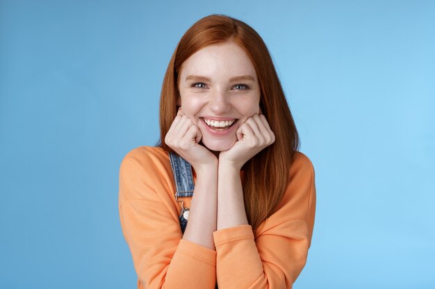 Entusiasmado atrevido boa aparência ruiva caucasiana magra palmas da cabeça olhar divertido intrigado ouvir história interessante satisfeito sorrindo rindo piadas bobas em pé fundo azul animado feliz