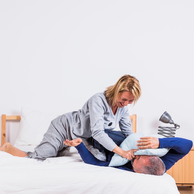 Envelhecido feliz mulher e homem se divertindo com almofadas na cama no quarto